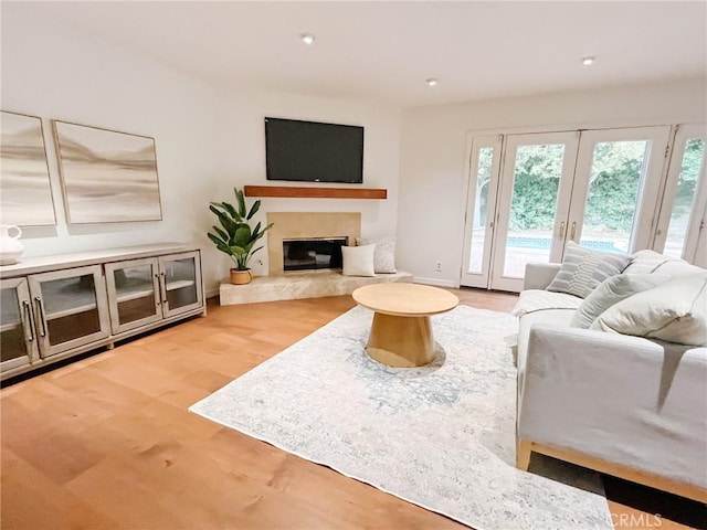 living area featuring french doors, baseboards, a fireplace, and light wood finished floors