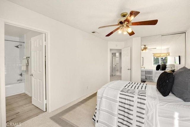 bedroom featuring light wood-type flooring, a ceiling fan, visible vents, and connected bathroom