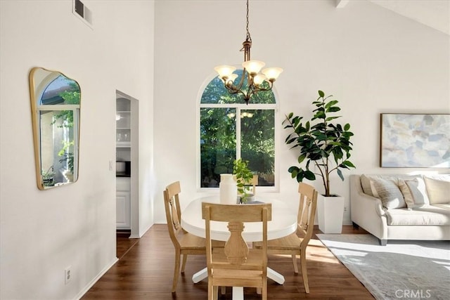 dining room with an inviting chandelier, wood finished floors, visible vents, and a towering ceiling