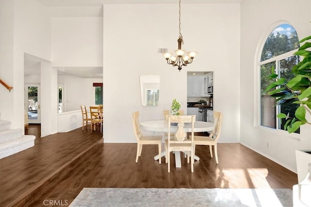 dining space featuring stairs, a high ceiling, wood finished floors, and a chandelier