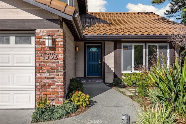 view of exterior entry with brick siding, an attached garage, and a tile roof