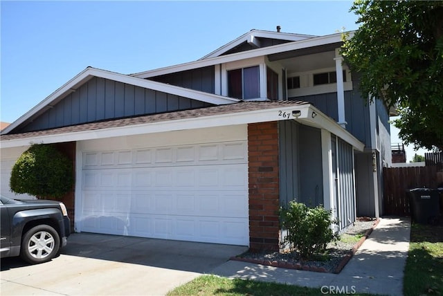 view of side of home featuring brick siding, an attached garage, board and batten siding, fence, and driveway