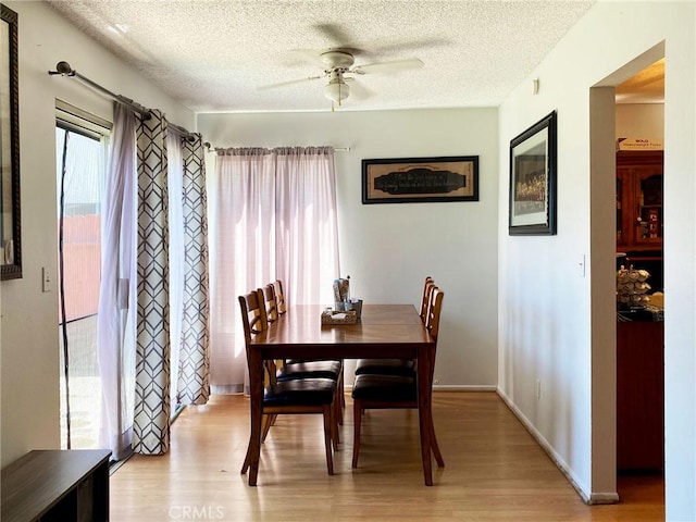 dining space featuring light wood-style flooring, baseboards, ceiling fan, and a textured ceiling