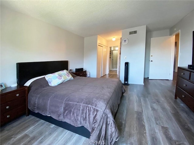 bedroom featuring a closet, visible vents, a textured ceiling, and wood finished floors