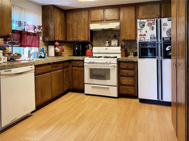 kitchen featuring tasteful backsplash, light wood-style floors, a sink, white appliances, and under cabinet range hood