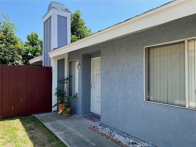 view of exterior entry featuring fence and stucco siding