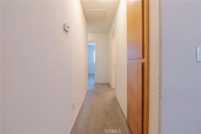 hall featuring baseboards, visible vents, and light colored carpet