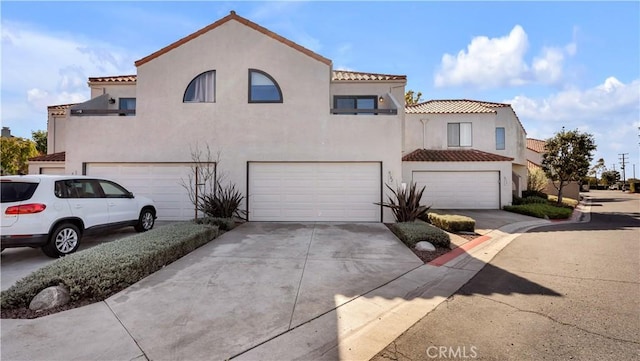 mediterranean / spanish-style house with a tiled roof, stucco siding, an attached garage, and concrete driveway