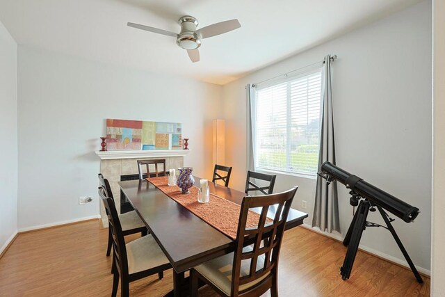 dining area with a fireplace, ceiling fan, baseboards, and wood finished floors