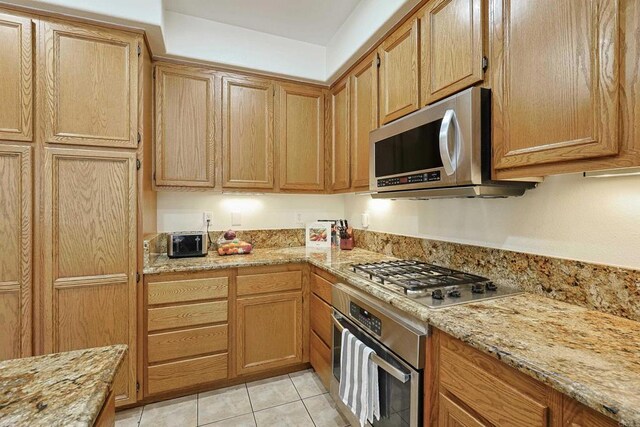 kitchen featuring light tile patterned floors, light stone counters, and stainless steel appliances