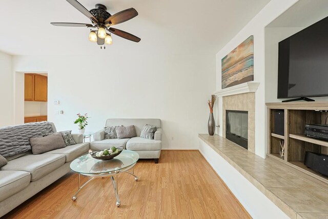 living area with a tiled fireplace, light wood-style floors, baseboards, and a ceiling fan