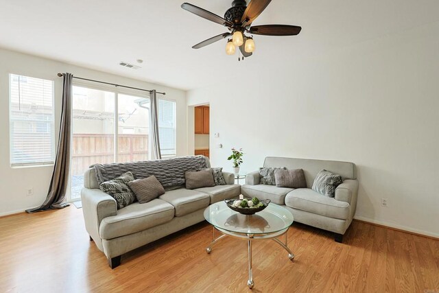 living area with baseboards, visible vents, light wood-type flooring, and a ceiling fan
