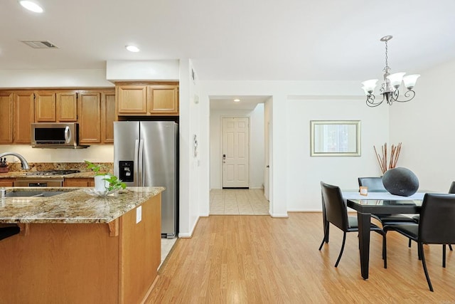 1582 Moonbeam Ln, Chula Vista, CA 91915 - kitchen featuring stainless steel appliances, brown cabinets, light stone counters, hanging light fixtures, and a chandelier