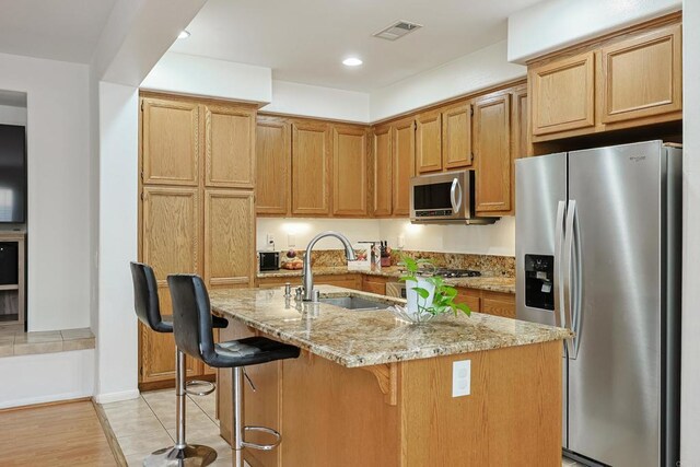 1582 Moonbeam Ln, Chula Vista, CA 91915 - kitchen featuring appliances with stainless steel finishes, a sink, light stone countertops, a breakfast bar, and an island with sink