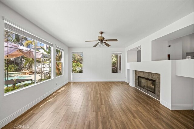 unfurnished living room with ceiling fan, baseboards, wood finished floors, and a glass covered fireplace