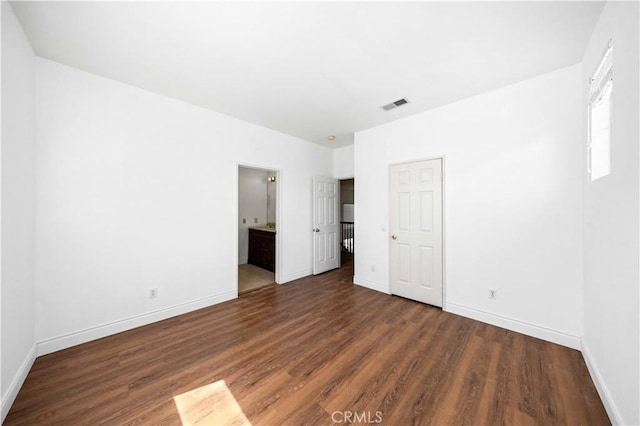 unfurnished bedroom with visible vents, connected bathroom, baseboards, and wood finished floors