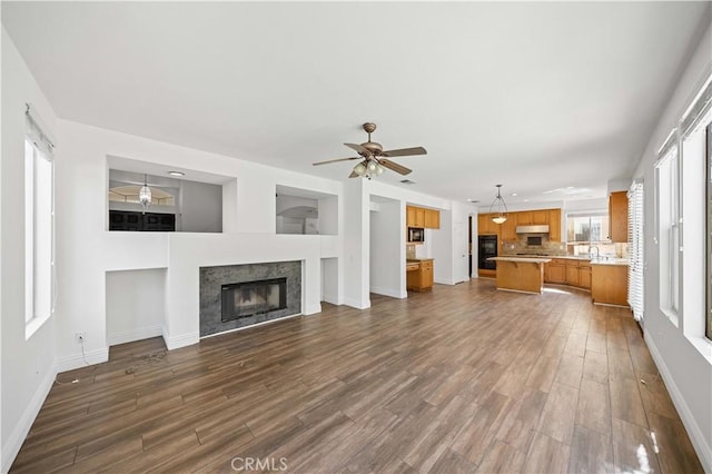 unfurnished living room with a glass covered fireplace, dark wood-style flooring, ceiling fan, and baseboards