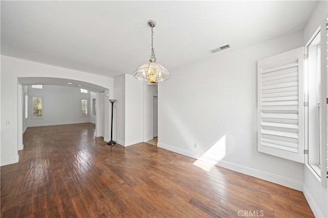 interior space with arched walkways, a chandelier, visible vents, baseboards, and wood-type flooring