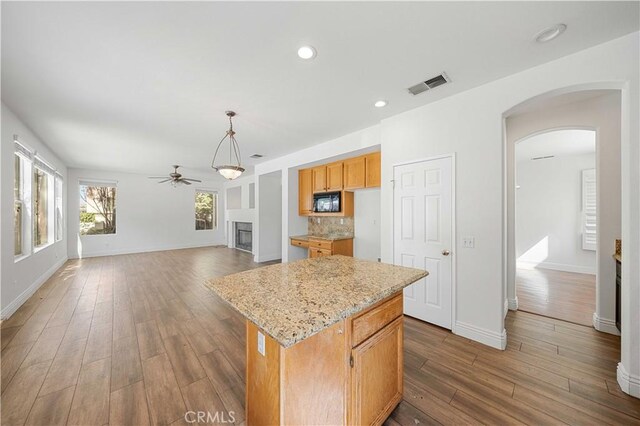 kitchen featuring arched walkways, a fireplace, wood finished floors, a kitchen island, and visible vents