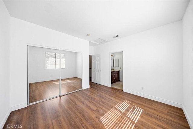 unfurnished bedroom with attic access, a closet, visible vents, and wood finished floors