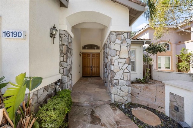 view of exterior entry featuring stone siding and stucco siding