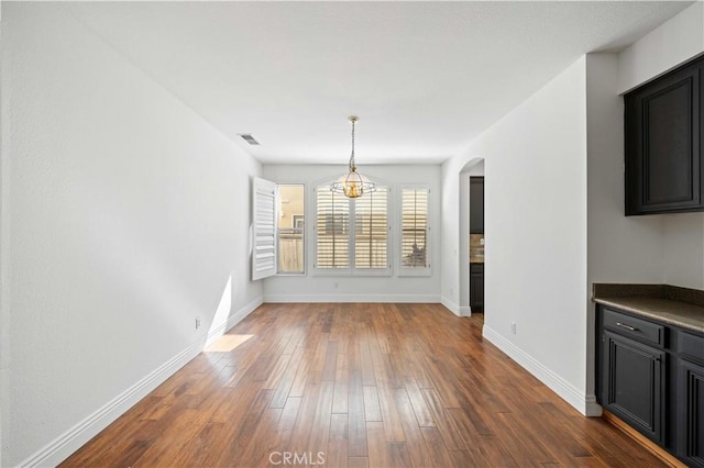 unfurnished dining area featuring arched walkways, dark wood-type flooring, visible vents, and baseboards