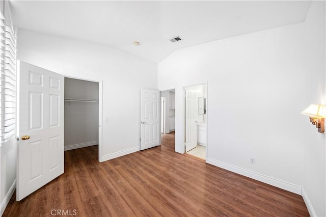 unfurnished bedroom with a walk in closet, visible vents, vaulted ceiling, wood finished floors, and baseboards