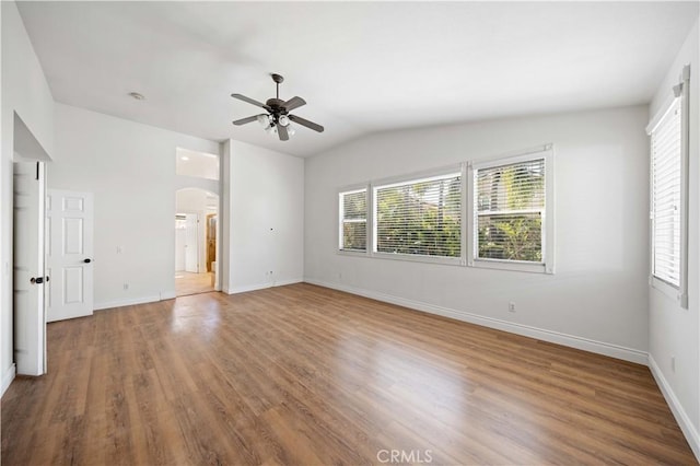 spare room featuring arched walkways, a healthy amount of sunlight, baseboards, and wood finished floors