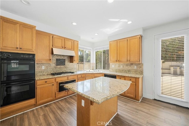 kitchen with under cabinet range hood, dobule oven black, a sink, and wood finished floors