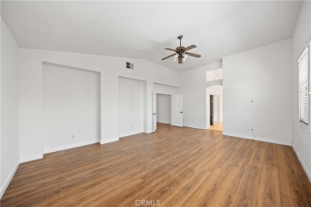 interior space featuring arched walkways, lofted ceiling, a ceiling fan, baseboards, and light wood-style floors