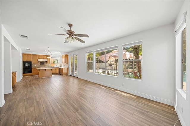 unfurnished living room with a ceiling fan, baseboards, visible vents, and wood finished floors