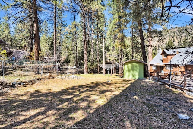 view of yard with a shed, an outdoor structure, fence, and a view of trees