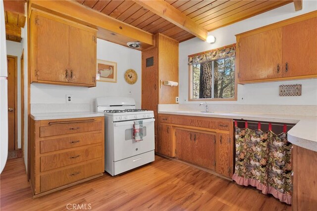 kitchen with gas range gas stove, a sink, light countertops, light wood finished floors, and beamed ceiling