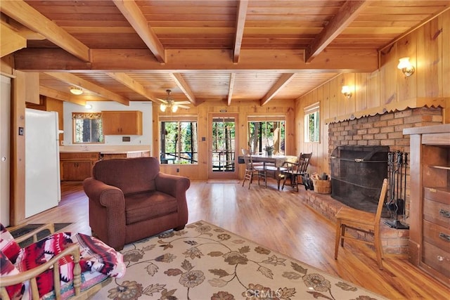 living area with light wood-style floors, a brick fireplace, wood ceiling, wooden walls, and beamed ceiling