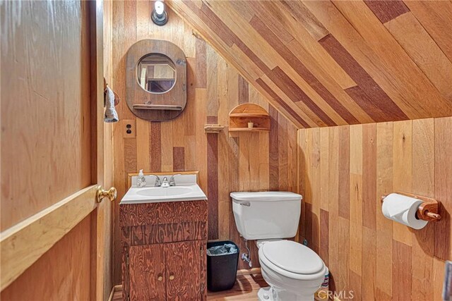 half bath featuring wood walls, vaulted ceiling, vanity, and toilet