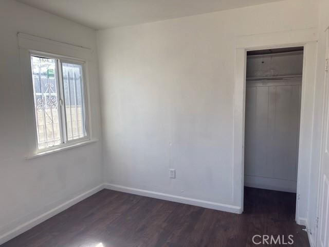 unfurnished bedroom with dark wood-style floors, a closet, and baseboards