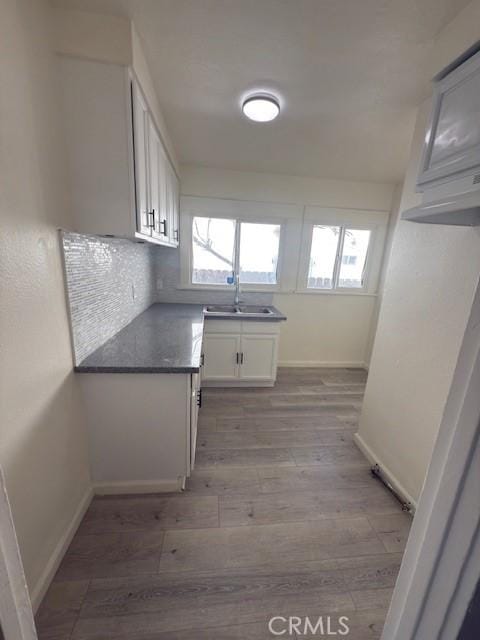 kitchen featuring light wood-type flooring, a healthy amount of sunlight, a sink, and dark countertops