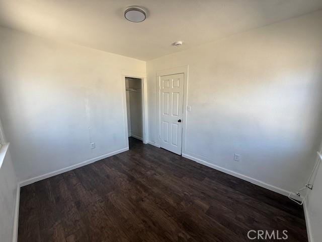 unfurnished bedroom with a closet, dark wood-style flooring, and baseboards