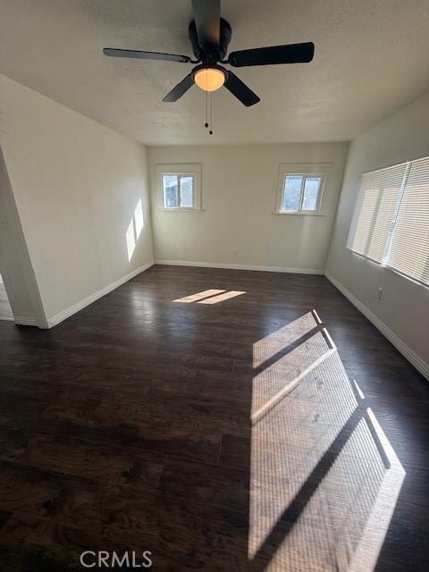 empty room featuring dark wood-style floors, ceiling fan, and baseboards