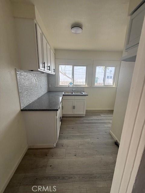 kitchen featuring light wood-type flooring, a wealth of natural light, white cabinetry, and a sink