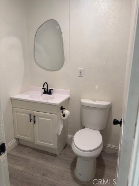 bathroom featuring toilet, baseboards, wood finished floors, and vanity