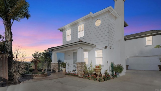 view of front of property featuring a chimney, stucco siding, a porch, a garage, and driveway