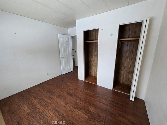 unfurnished bedroom with wood finished floors and two closets