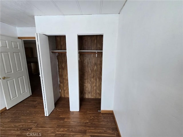 unfurnished bedroom featuring multiple closets and dark wood-style flooring