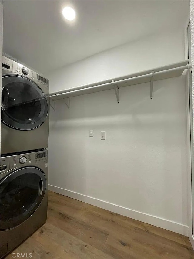 washroom with laundry area, light wood-type flooring, stacked washer / drying machine, and baseboards