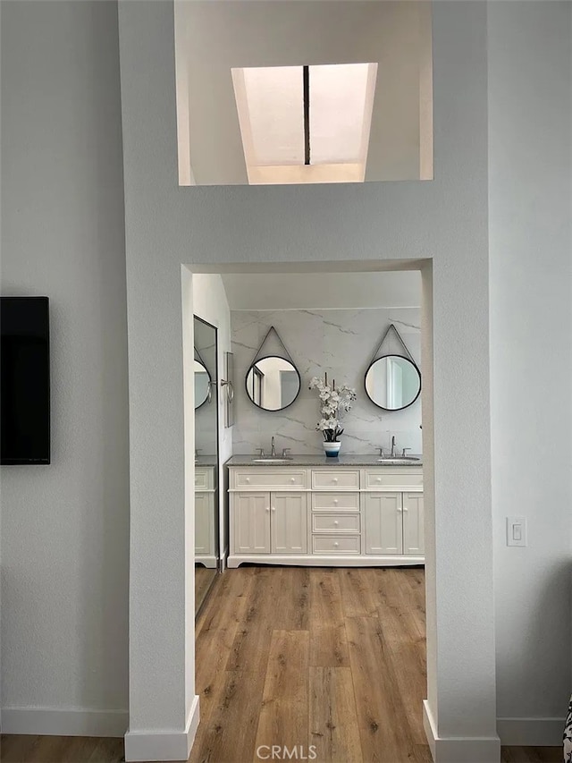 hall with wood finished floors, baseboards, and a sink