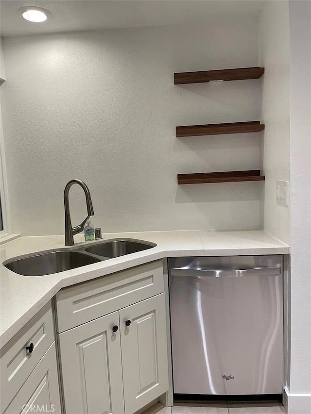 kitchen with stainless steel dishwasher, light countertops, white cabinets, and a sink