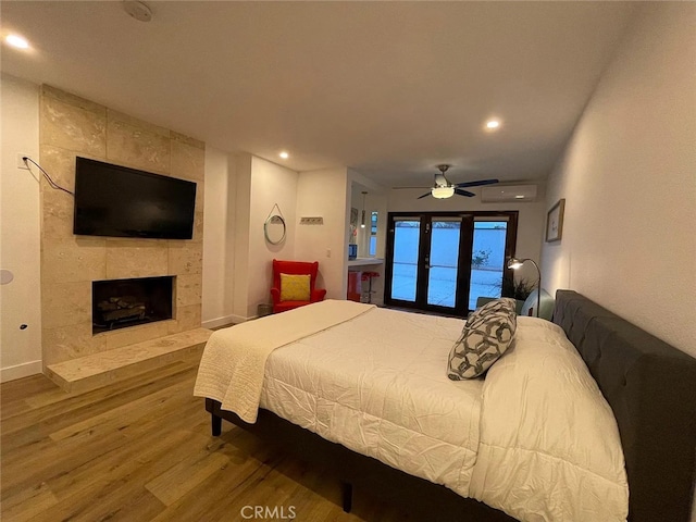 bedroom featuring a wall mounted air conditioner, a tiled fireplace, wood finished floors, recessed lighting, and baseboards