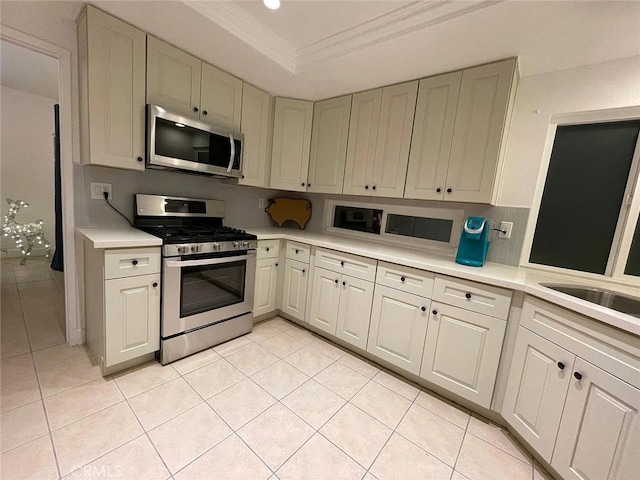 kitchen with a tray ceiling, crown molding, light countertops, and appliances with stainless steel finishes