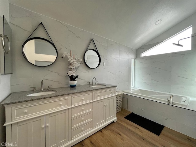 full bathroom with tile walls, wood finished floors, lofted ceiling, and a sink